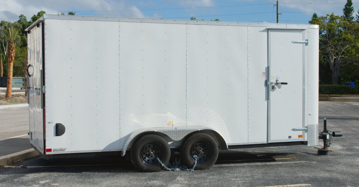 Side view of a white tandem-axle enclosed cargo trailer parked on a lot